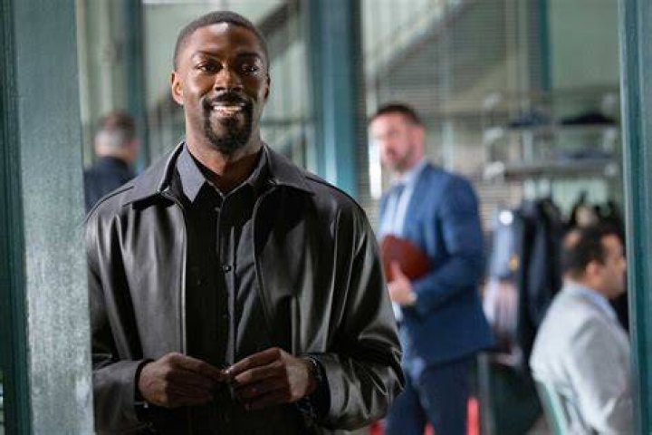 David Ajala in a black t-shirt poses for a picture.