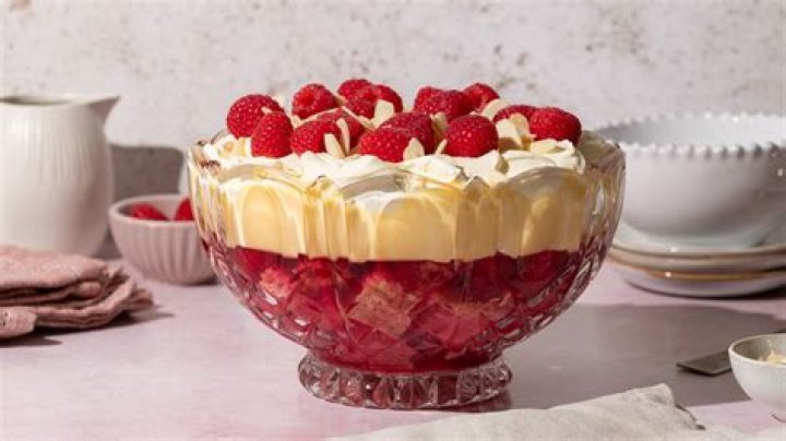 Trifle dish with cake, whipped cream, jam and raspberries.